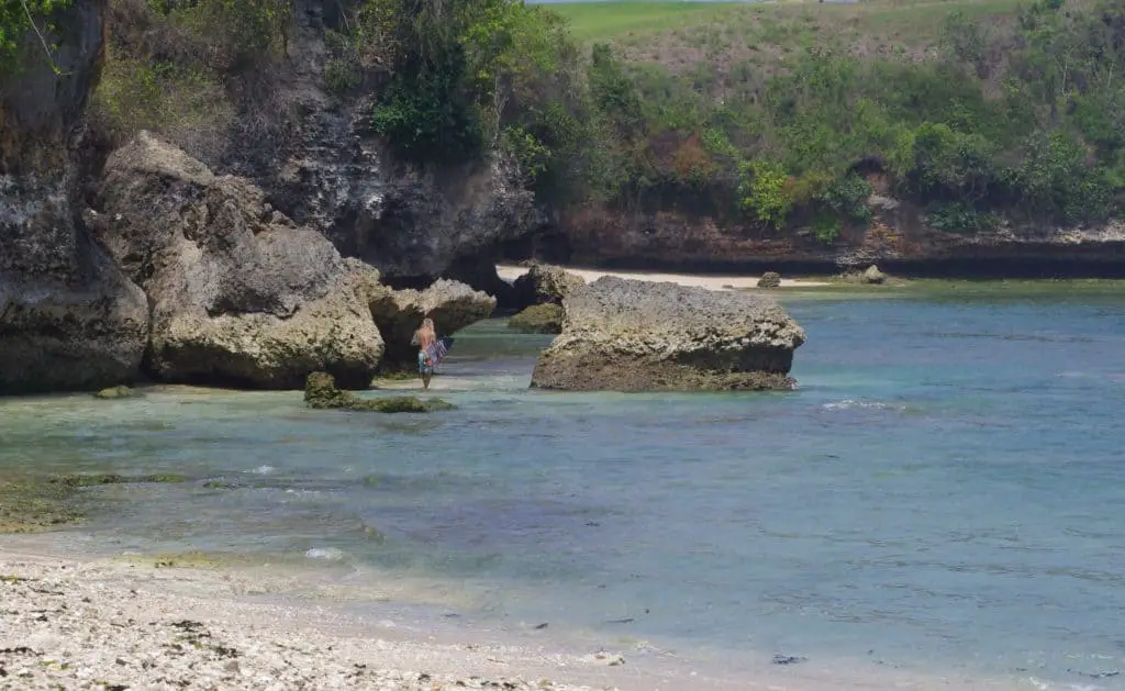 a surfer is walking between the rocks at Balangan beach on his way to the pipeline