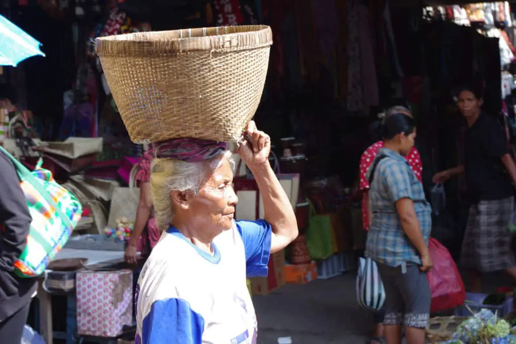 balinese woman walking with a basket on her head in ubud