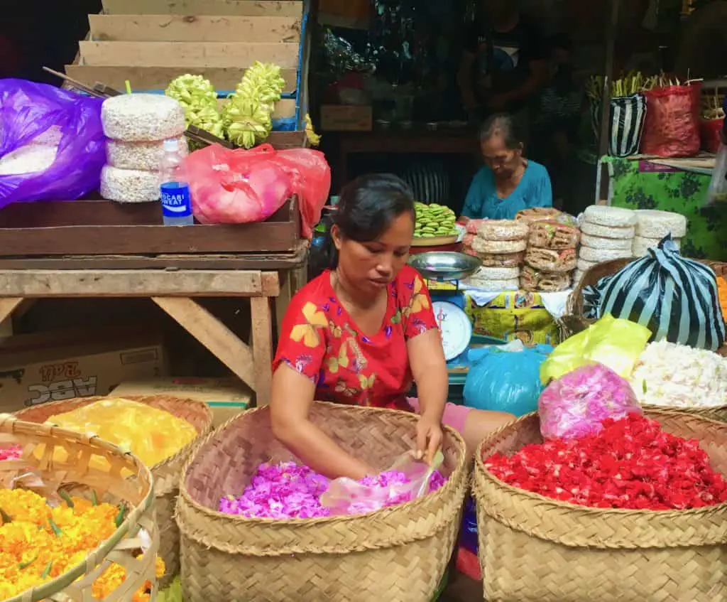 balinese woman preparing a bag of purple flower petals at the ubud market