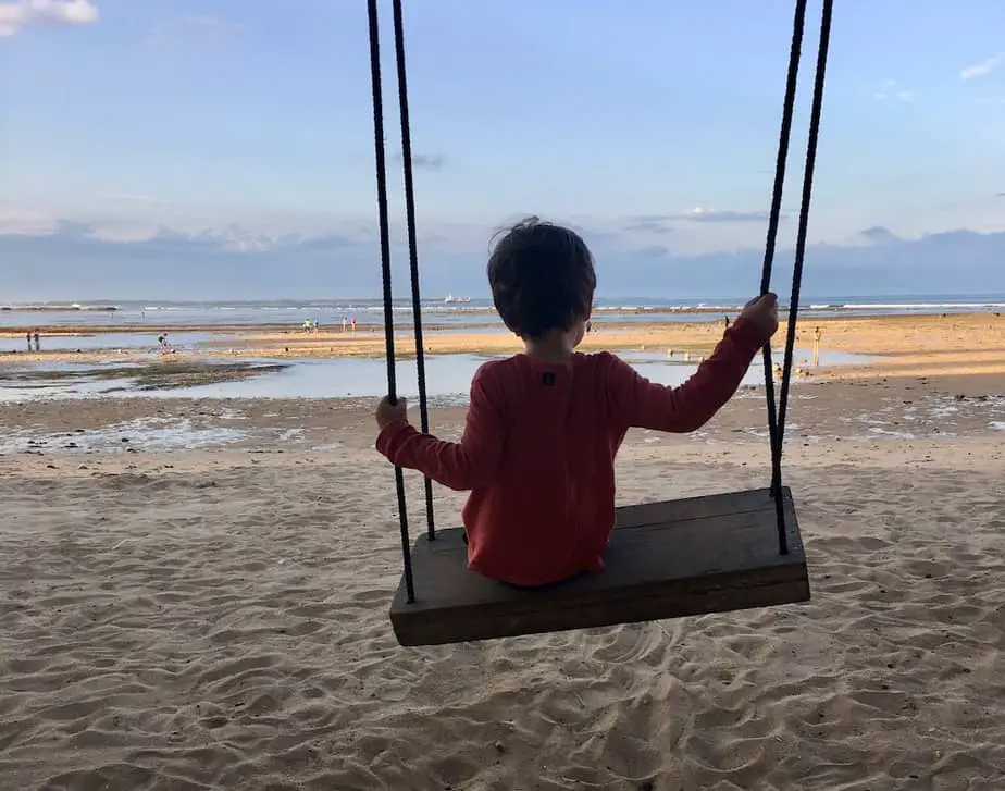little boy on a swing in Nusa Dua beach during low-tide