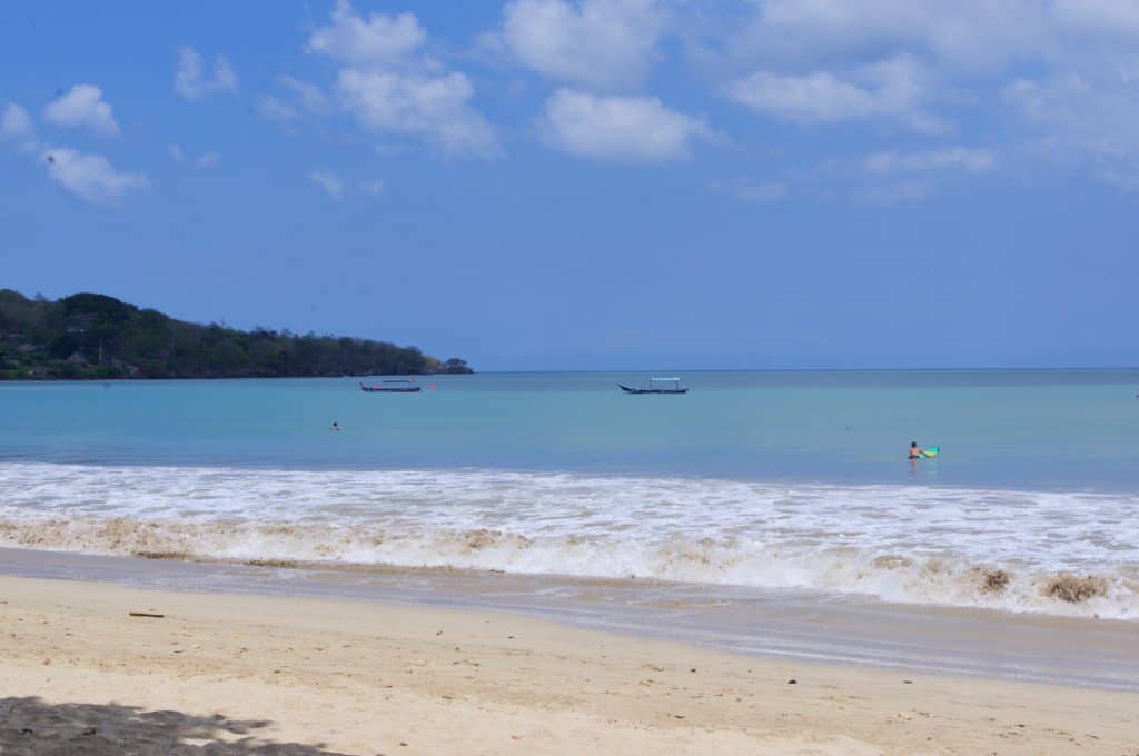 a couple of boats and a surfer in the water at jimbaran bay