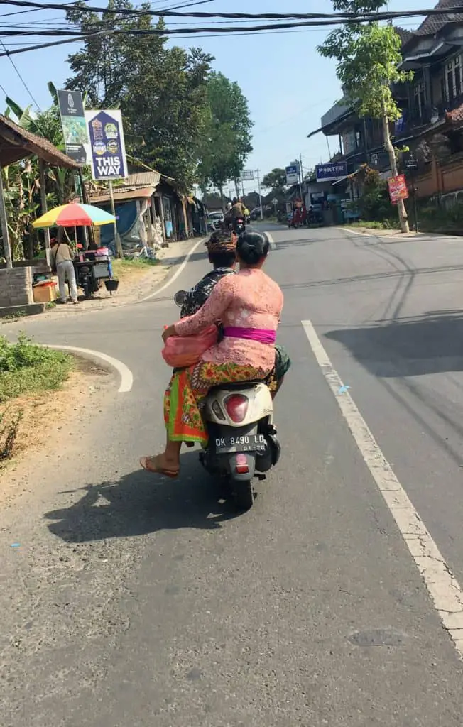 balinese woman sitting in colourful clothing at the back of the motor bike