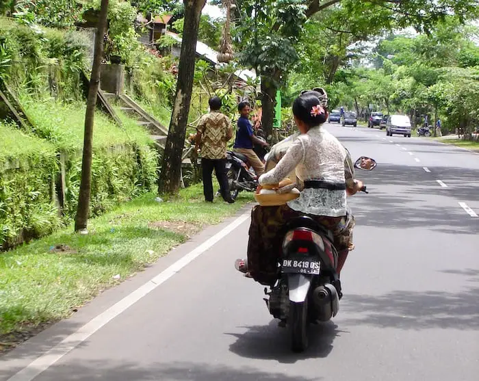 balinese woman with offerings on the back of a motor bike